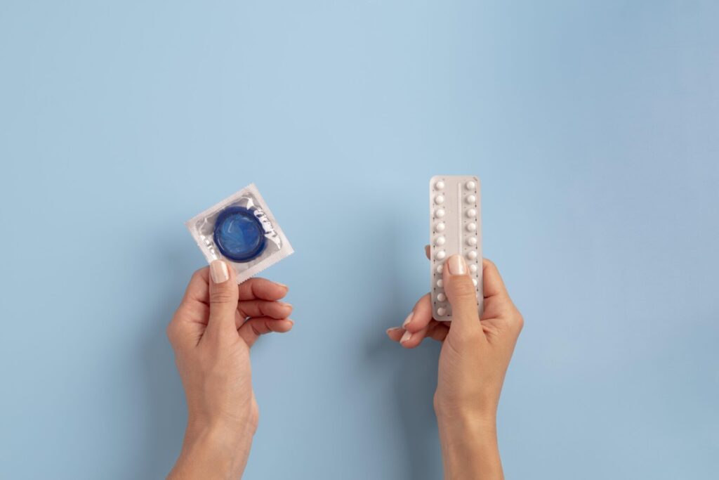 Birth control comparison showing a condom and birth control pills held in hands
