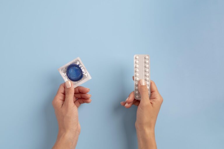 Birth control comparison showing a condom and birth control pills held in hands