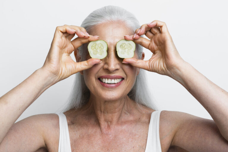 Older adult smiling with cucumber slices over her eyes, representing Slow Aging and healthy aging through balanced lifestyle habits.